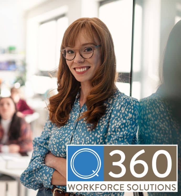 Redhead teacher smiling in a blue blouse at the front of her classroom
