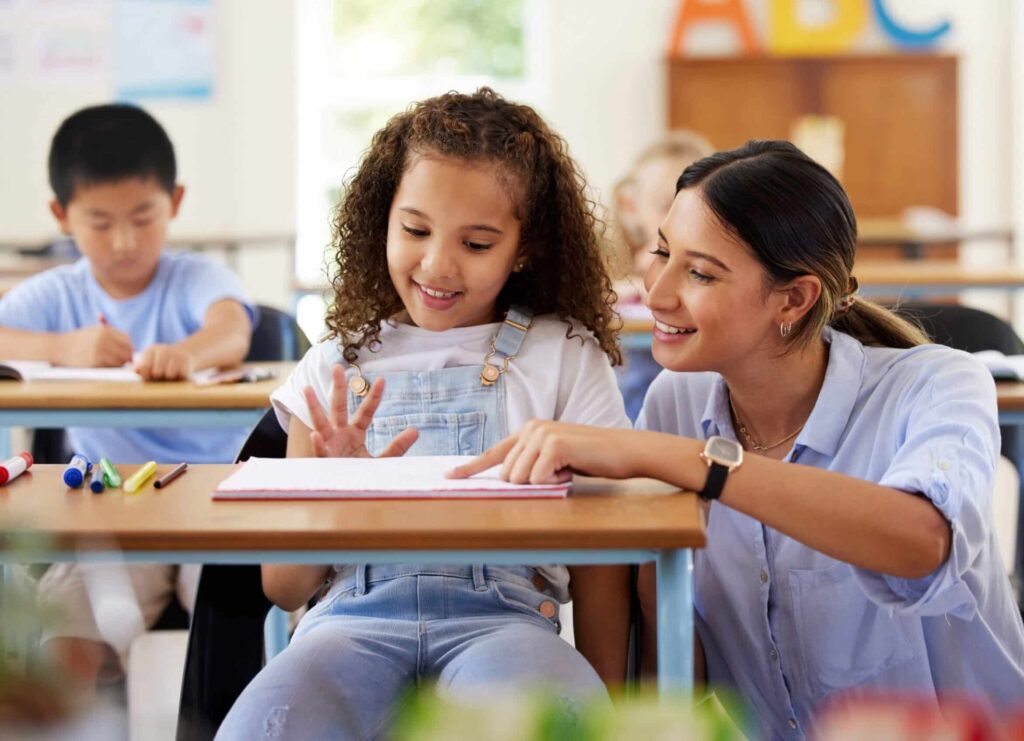 A teacher knelt down beside a student at their desk