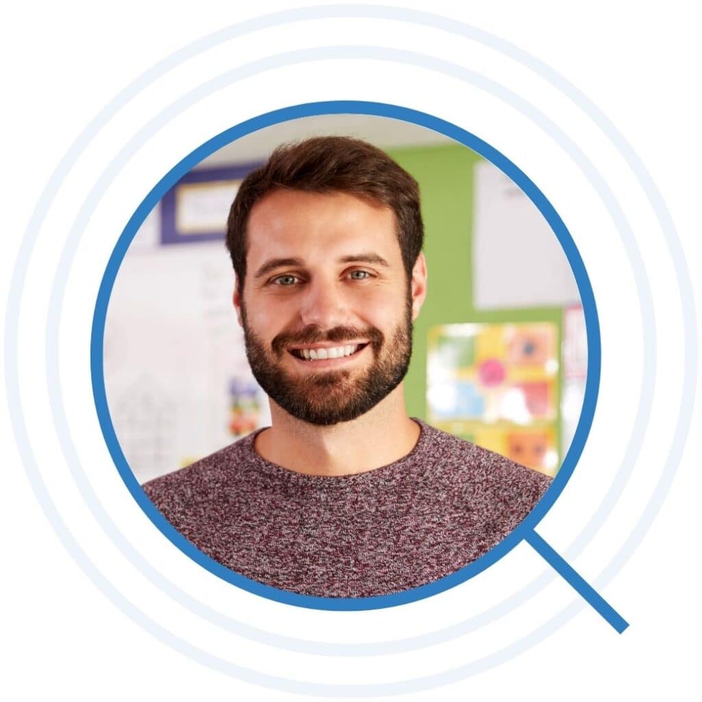 Bearded teacher smiling in front of a bulletin board