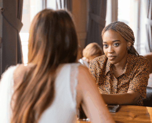 Two women sit across from each other at a table, engaged in a serious conversation.