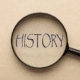 Magnifying glass focusing on the word 'HISTORY' written in bold letters on a beige background.