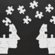 Two human heads made of white puzzle pieces facing each other on a black background, with several puzzle pieces floating between them, symbolizing knowledge transfer, communication, or shared understanding.